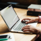 Eine Person arbeitet an einem Laptop auf einem Schreibtisch – Symbolmotiv für die Nutzung von Online-Services am Computer.